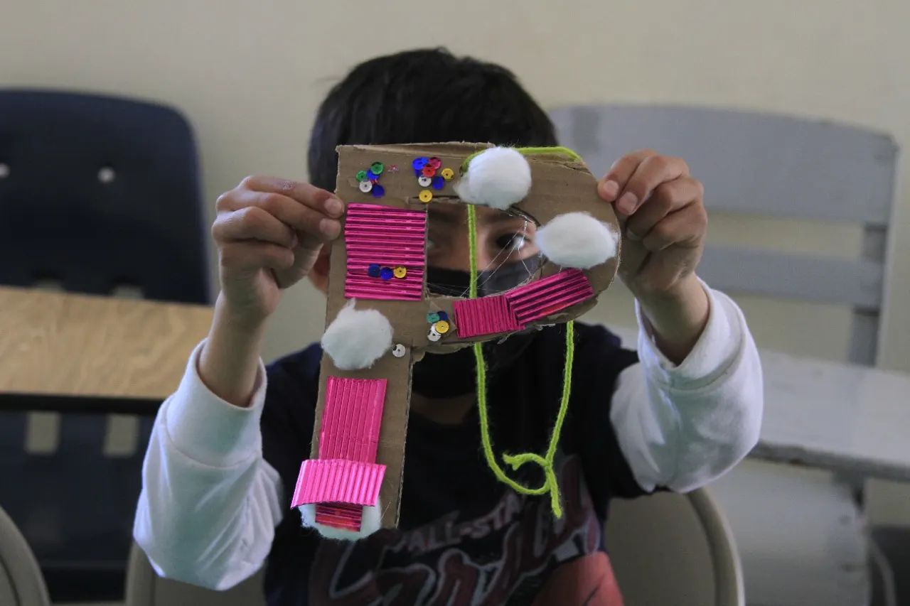 Niña muestra una creación de cartón y colores en un taller